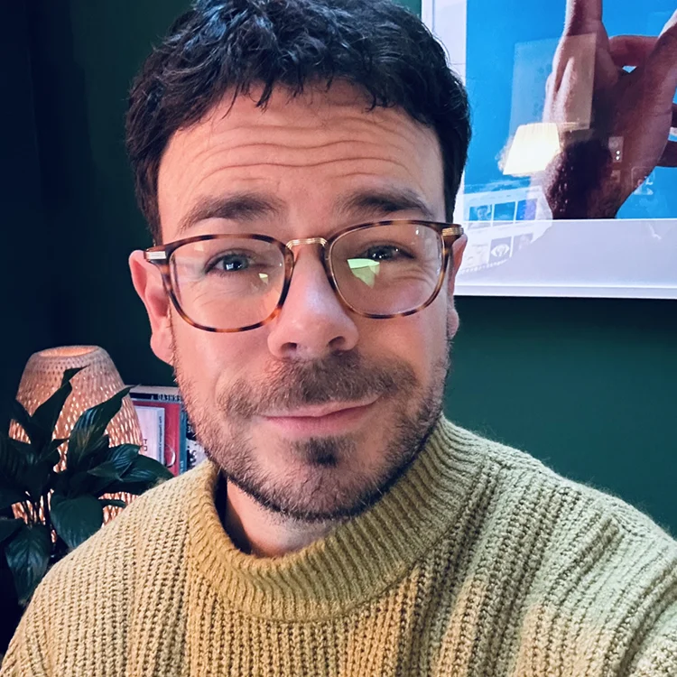 Portrait von Boris Jakob in einem warmen Raum. Er trägt eine Brille und einen gelben Strickpullover und blickt freundlich in die Kamera.