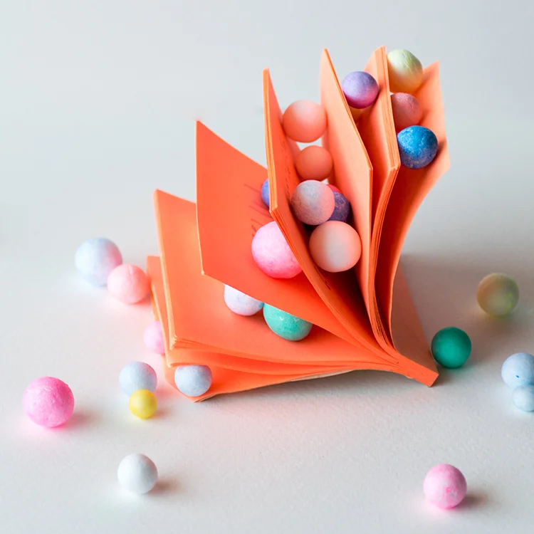 Gefaltetes orangefarbenes Papier mit farbigen Kugeln als visuelle Metapher für Priorisierung und sinnvollen Einsatz eines begrenzten Design-Budgets.